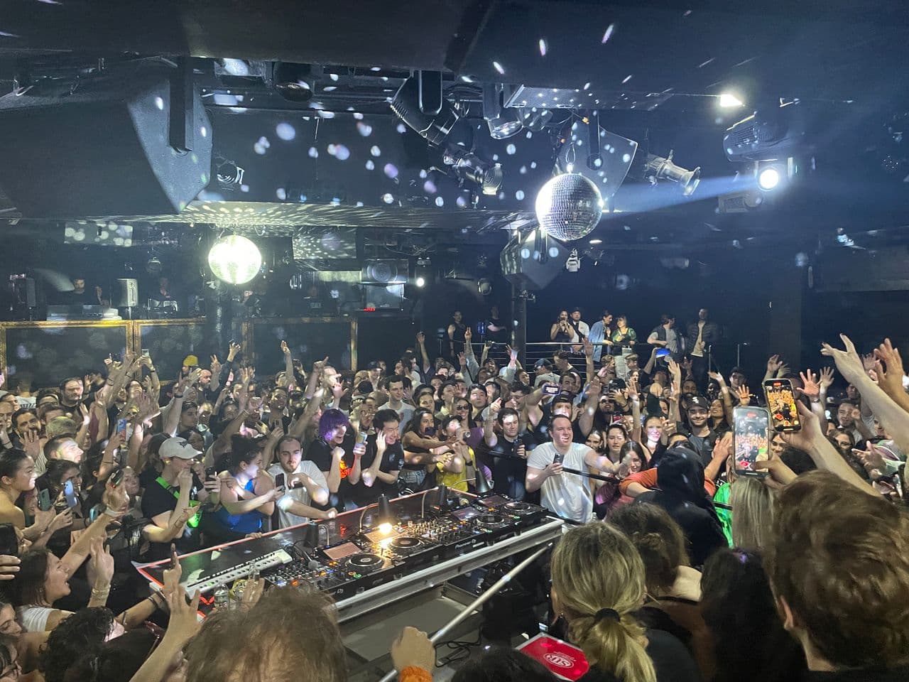 Flash-lit ravers surrounding a DJ booth