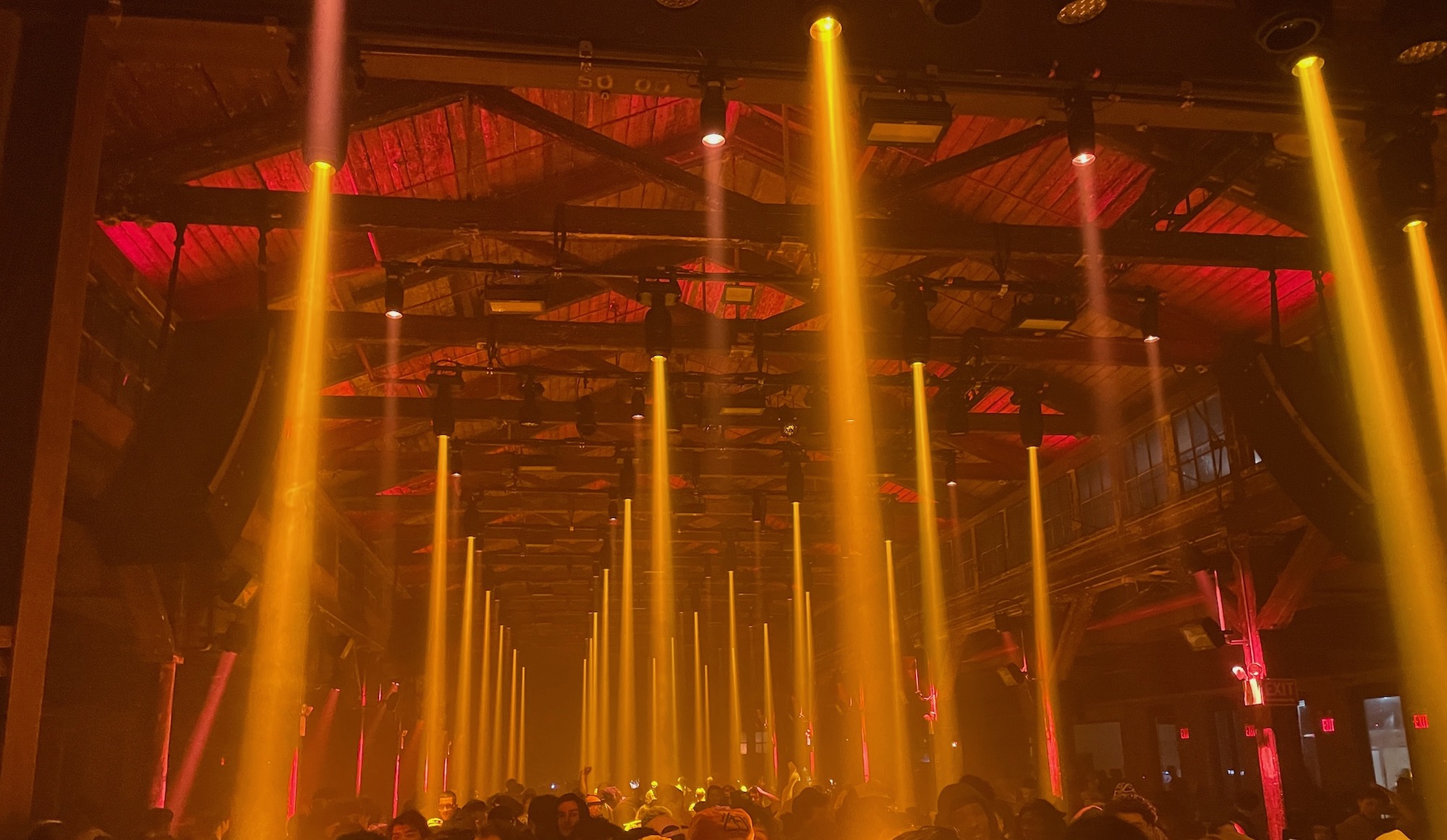 Orange light beams filling a packed Brooklyn warehouse rave